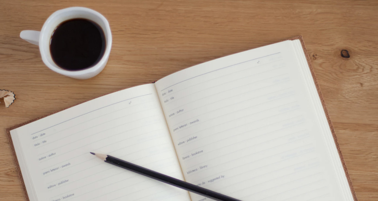 Coffee on a table with an opend jurnaling book and a pen