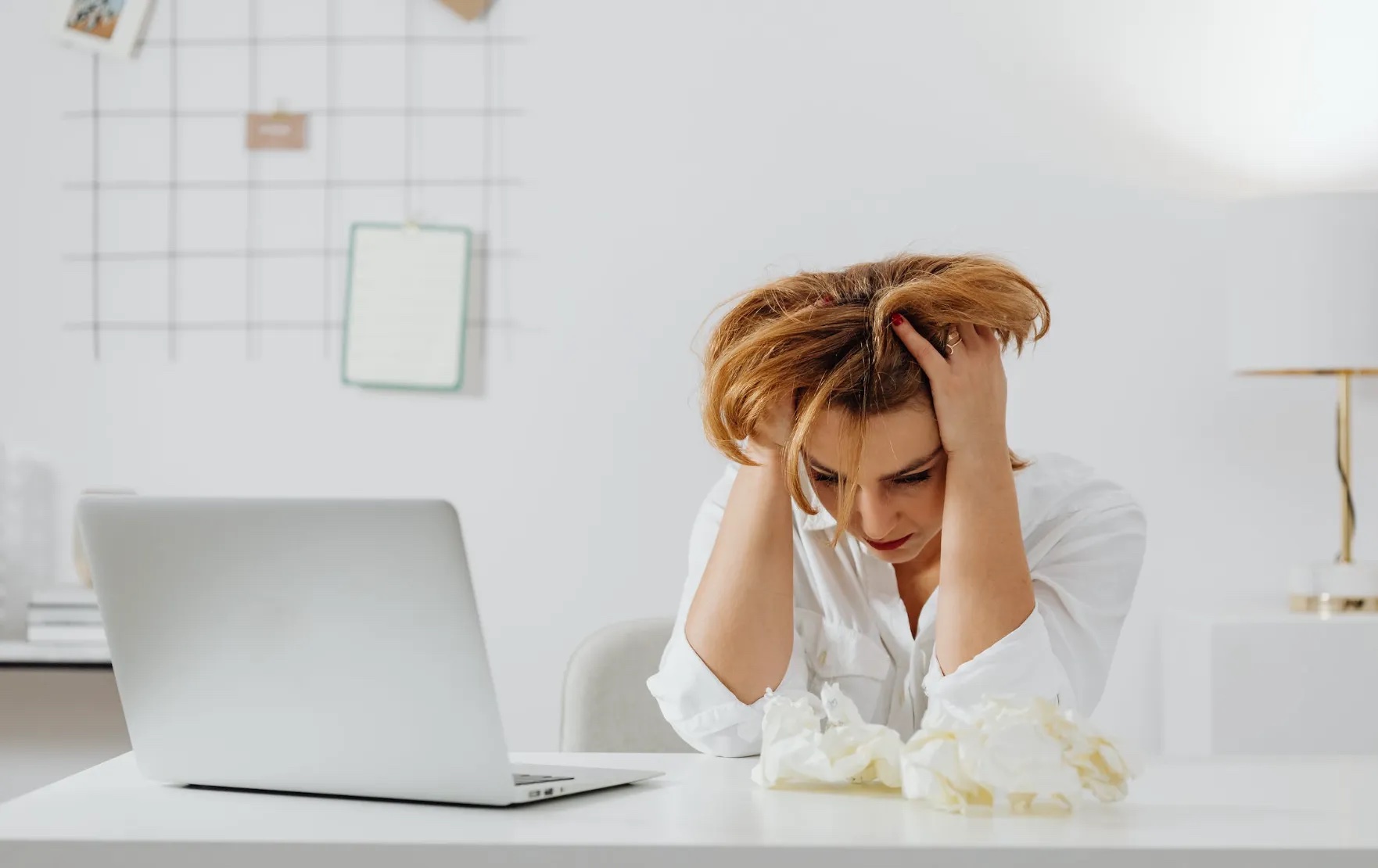 Woman sitting at a laptop, holding her head. Image: Pexels - Karolina Grabowska