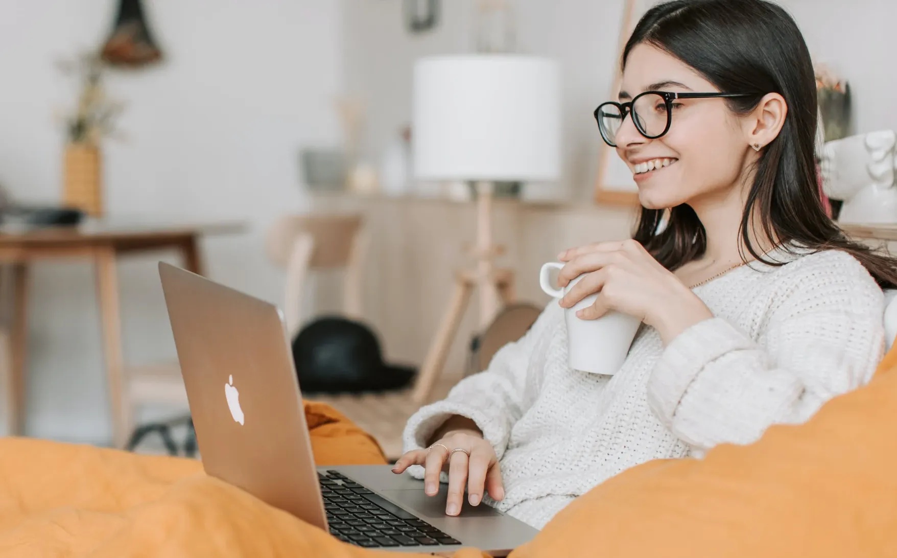 Woman sitting at a laptop with a beverage in her hand, smileing.