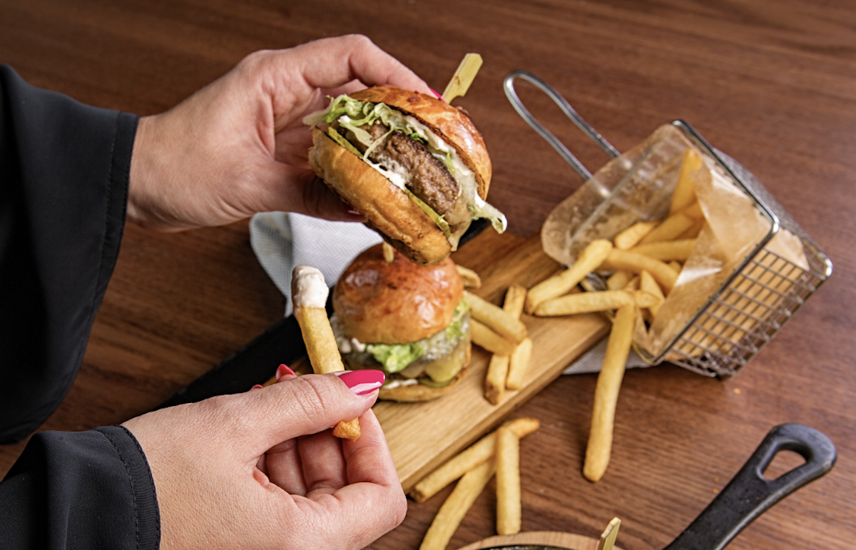 Person eating hamburger and fries. Image: Pexels - Denys Gromov