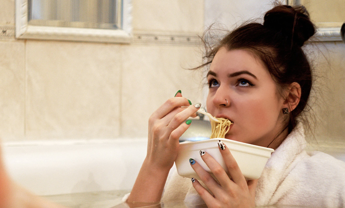 Girl sitting in tub eating a bowl of pasta looking sad. 