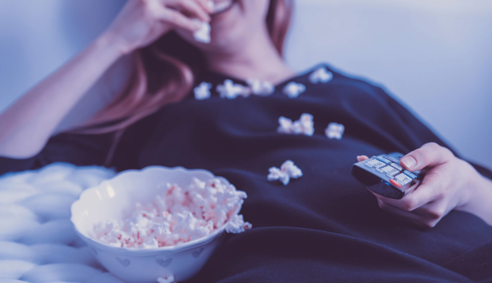 Girl eating popcorn from the couch and watching TV. 