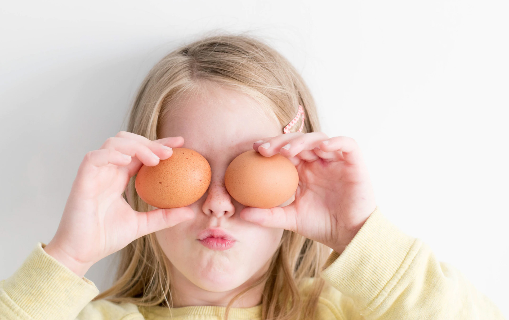 child holding 2 eggs in front of her eyes 