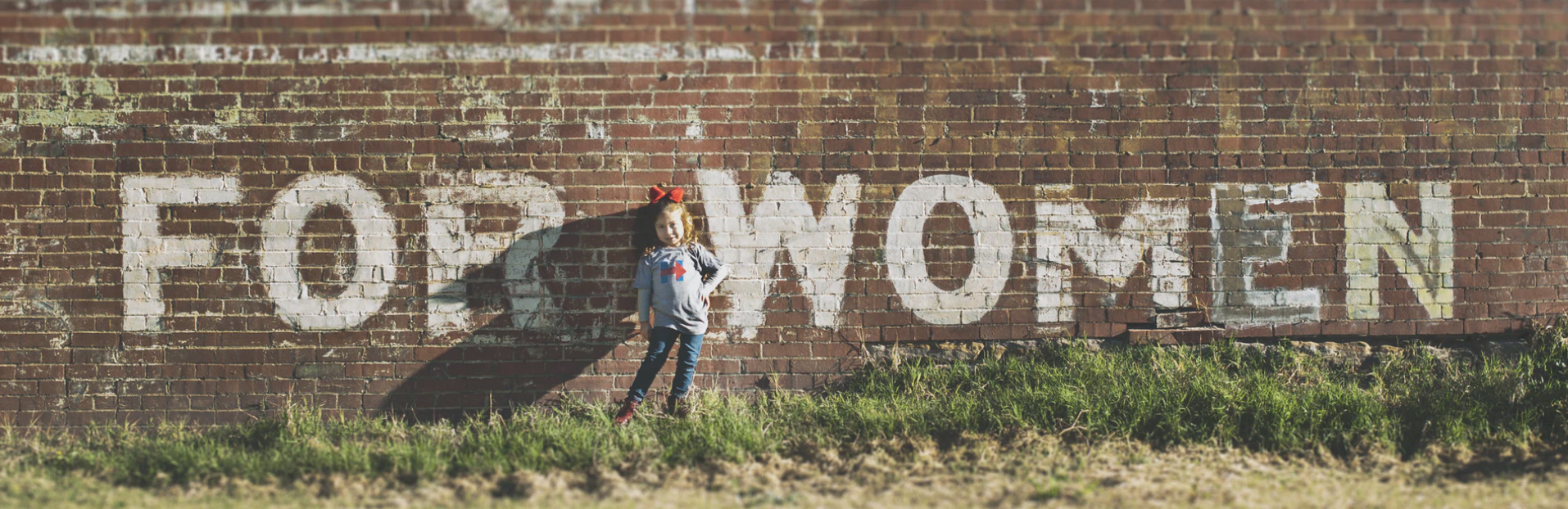 A sign on a brick wall that reads for women with a little girl standing in front of it 