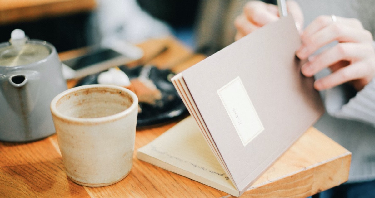 Woman journaling in a coffee shop. Unsplash - Daria Shevtsova