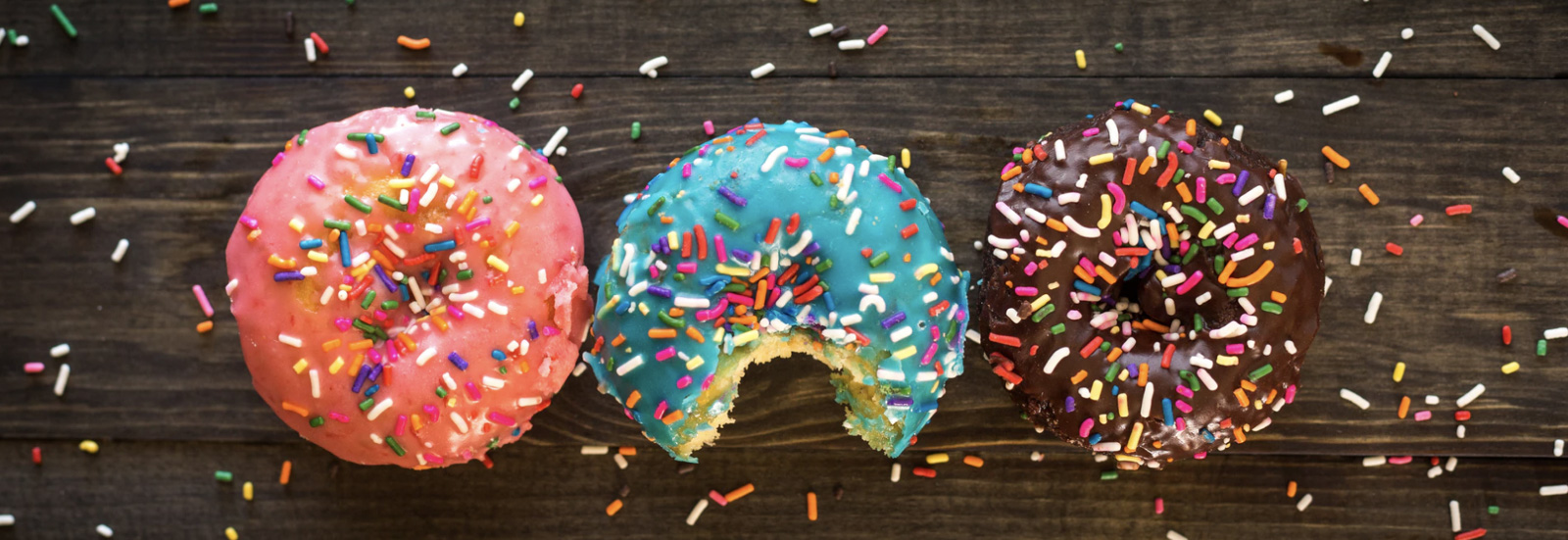 Three donuts with sprinkles on a table next to each other.