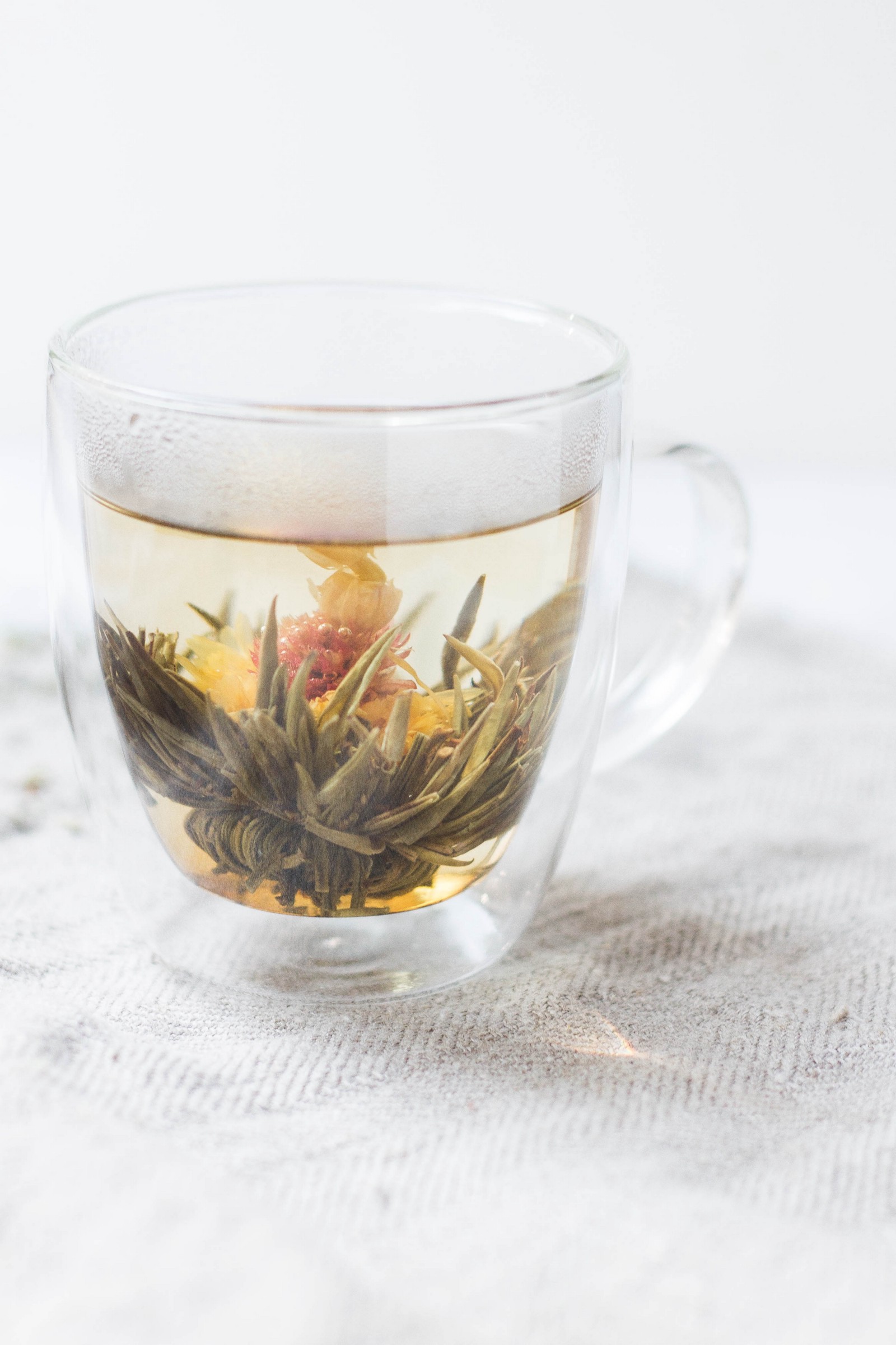 A cup of green loose leaf tea in a see through glass mug. 