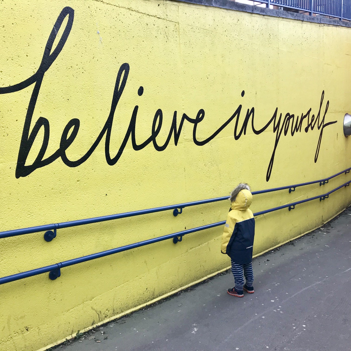 A yellow wall with believe in yourself written on it with a child looking up at it