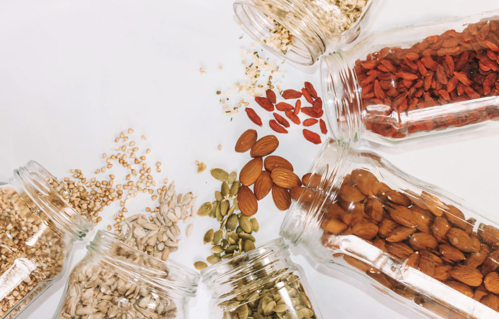 Five jars of nuts spilled out with sunflower seeds and other seeds