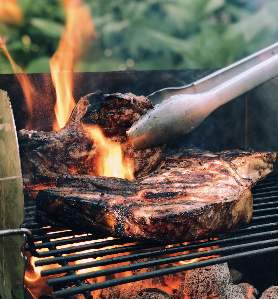 Red meat, steak, being prepared on an open grill with open flames.