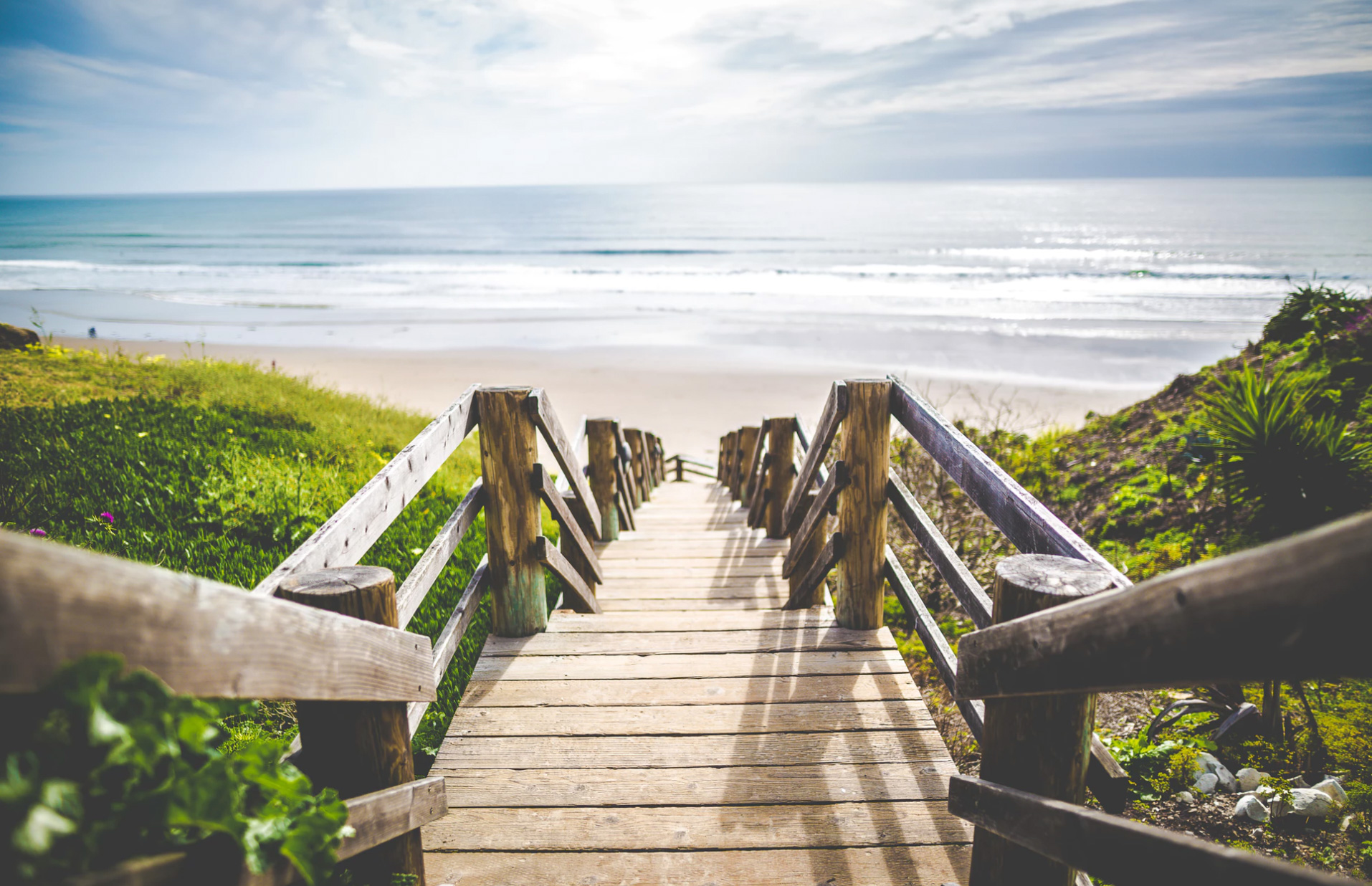 A beach scenery with wooden stairs going down to the water. 