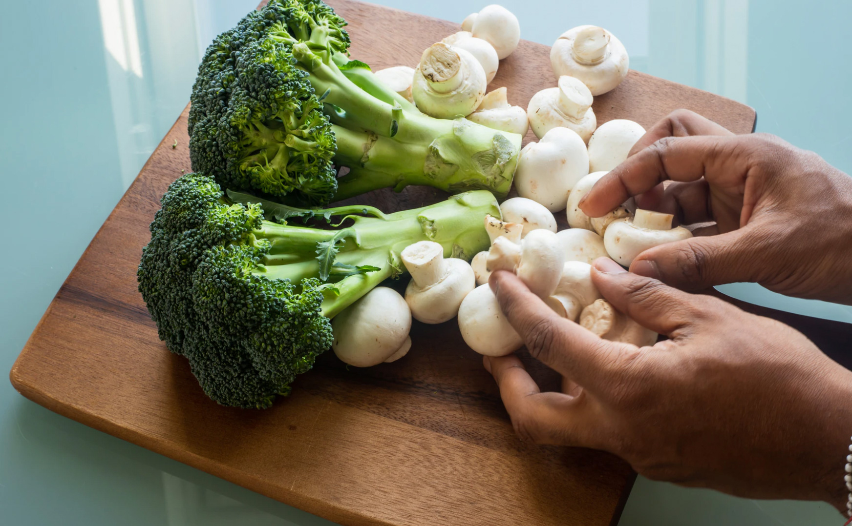 Person cutting and cleaning mushrooms and broccoli 