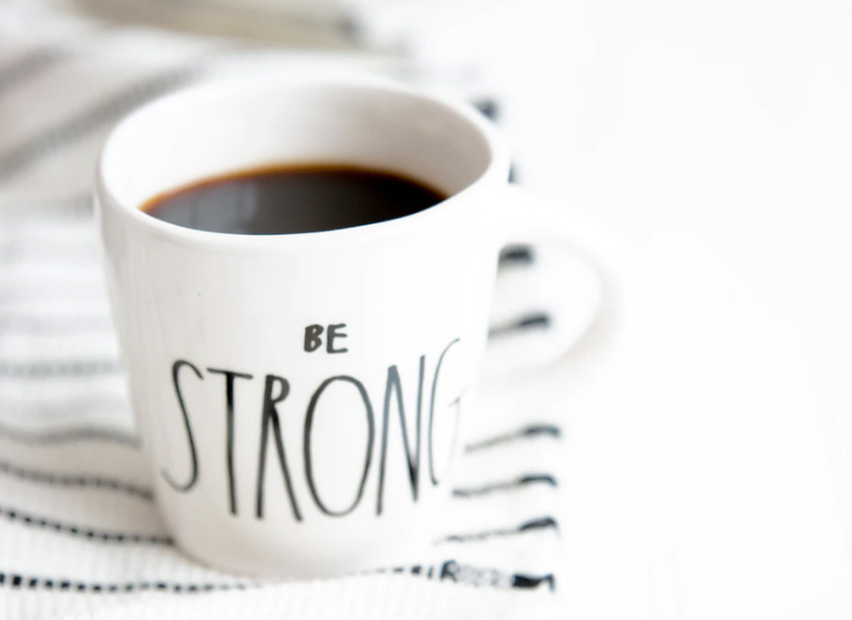 A cup of coffee inside of a mug that says be strong. 