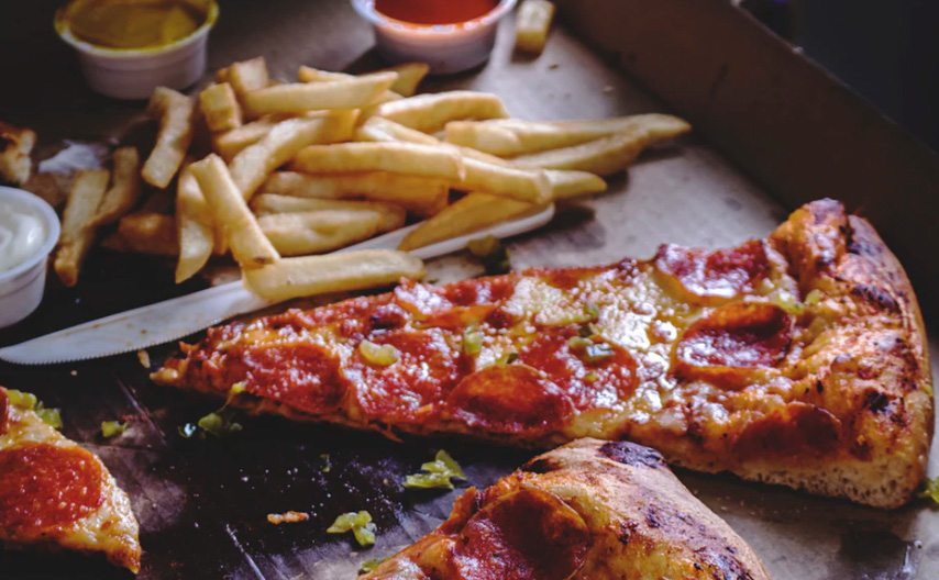 A pizza box with some pizza and french fries 